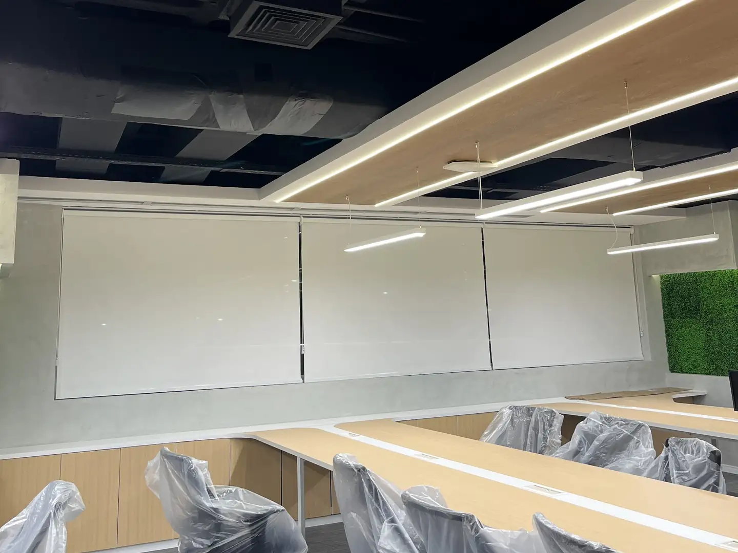 Telas solares em rolô fechadas ao longo da parede de um escritório com estações de trabalho