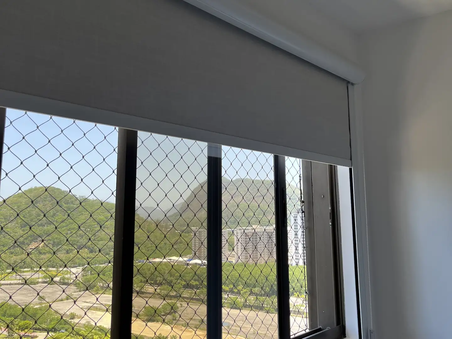 Persiana rolô meio recolhida em uma janela com vista para a serra