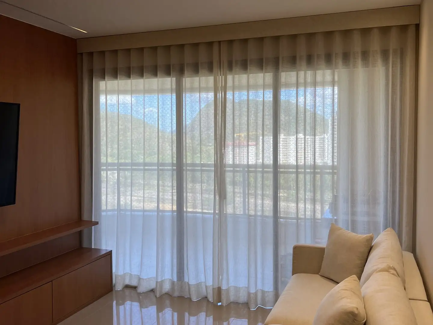 Cortinas e persianas da Astrale Decor: sala com voil do teto ao piso e vista para a serra