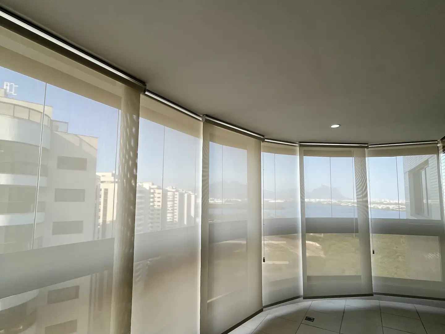 Área de atendimento da Astrale Decor: varanda curva com telas solares que deixam ver os prédios e o céu