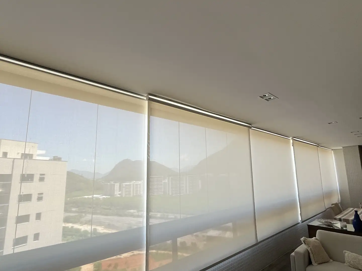 Telas solares em uma varanda integrada à sala, com vista para a serra. Cortinas e persianas no Rio de Janeiro, pela Astrale Decor