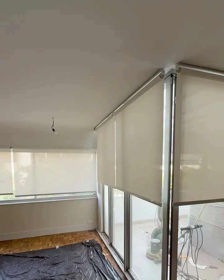 Telas solares em rolô a meia altura em uma sala com janelas em dois lados