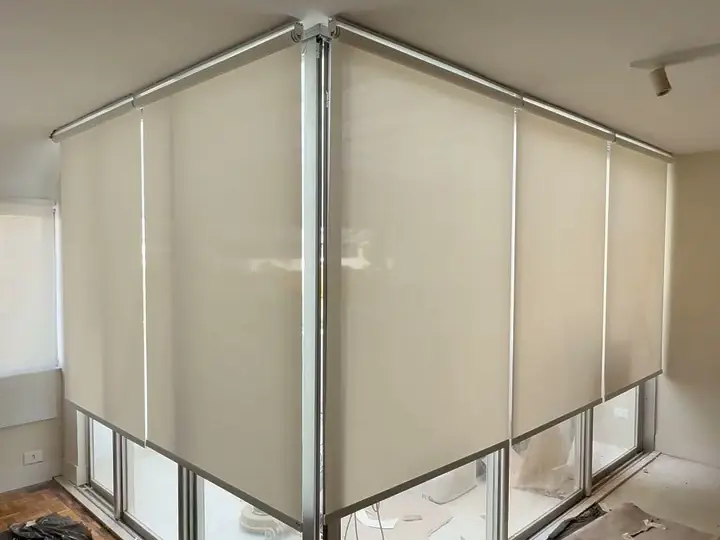 Telas solares em rolô fechadas no canto envidraçado de uma sala