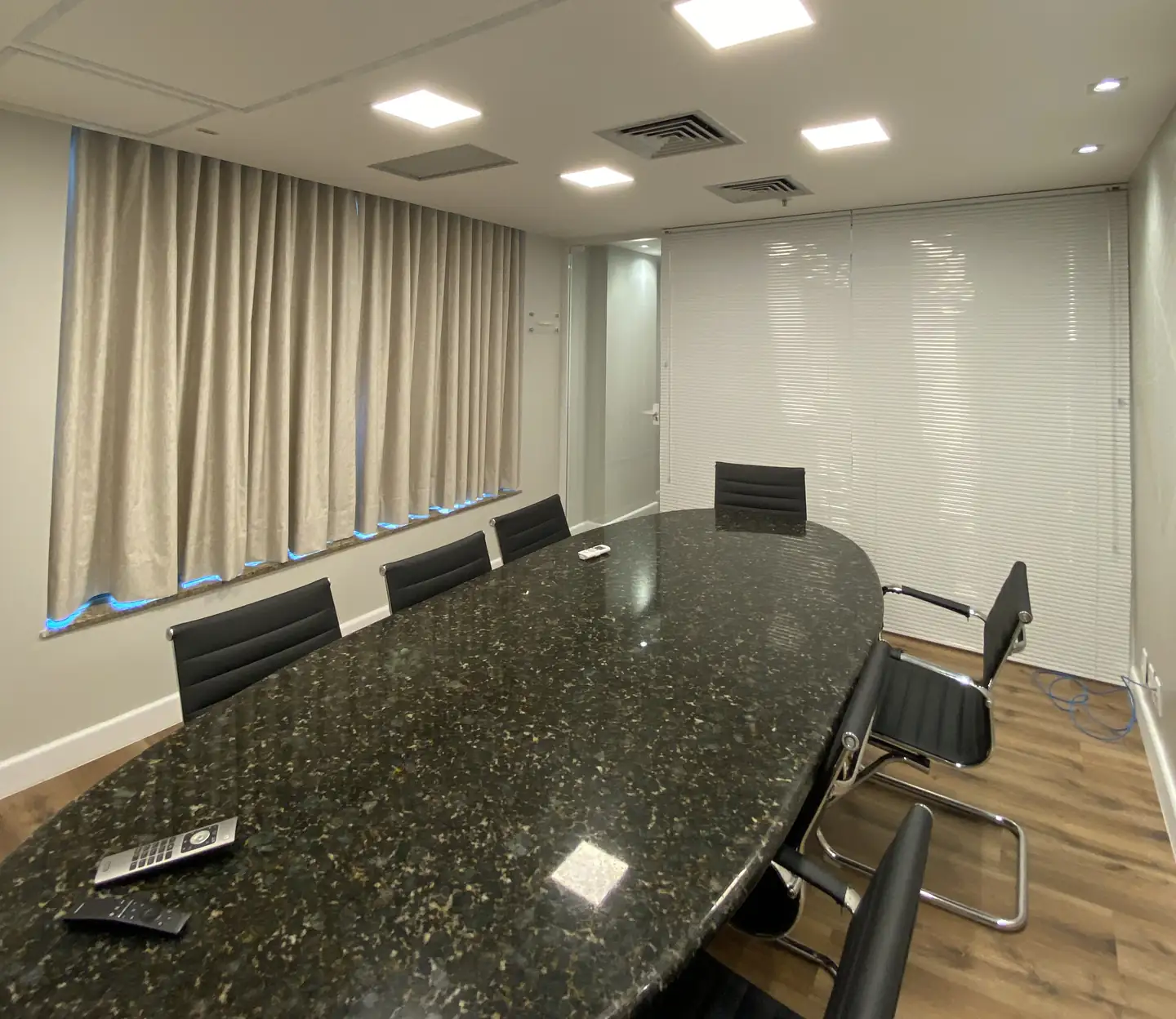 Sala de reunião com cortinas de tecido em tom areia e mesa de granito