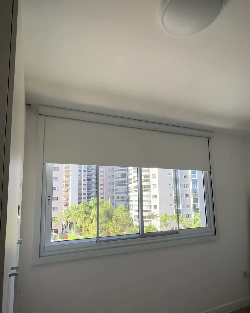 Quarto com persiana rolô blackout motorizada descendo entre guias laterais