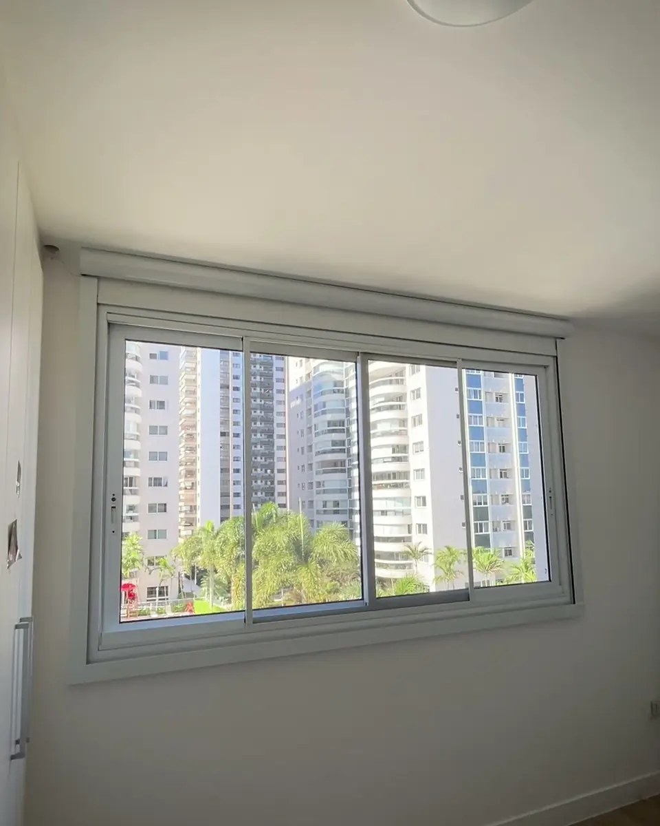 Blackout motorizado com guias em quarto: janela de quarto com a persiana blackout recolhida e os prédios à vista