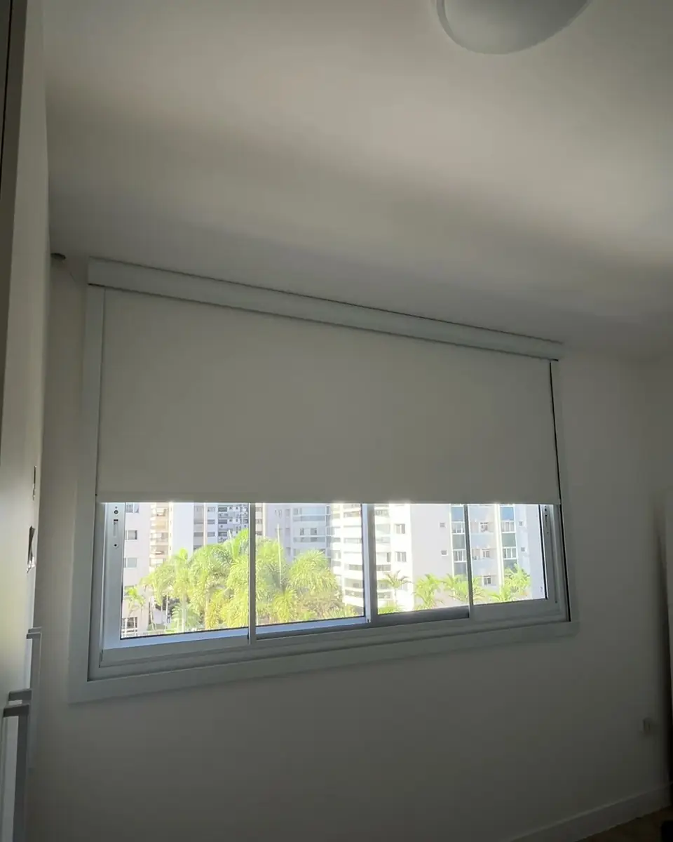 Persiana blackout com guias quase fechada, com uma faixa de luz na base