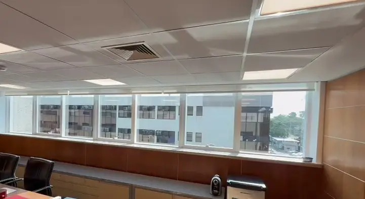 Sala de reunião com as telas solares recolhidas e os prédios vizinhos à vista