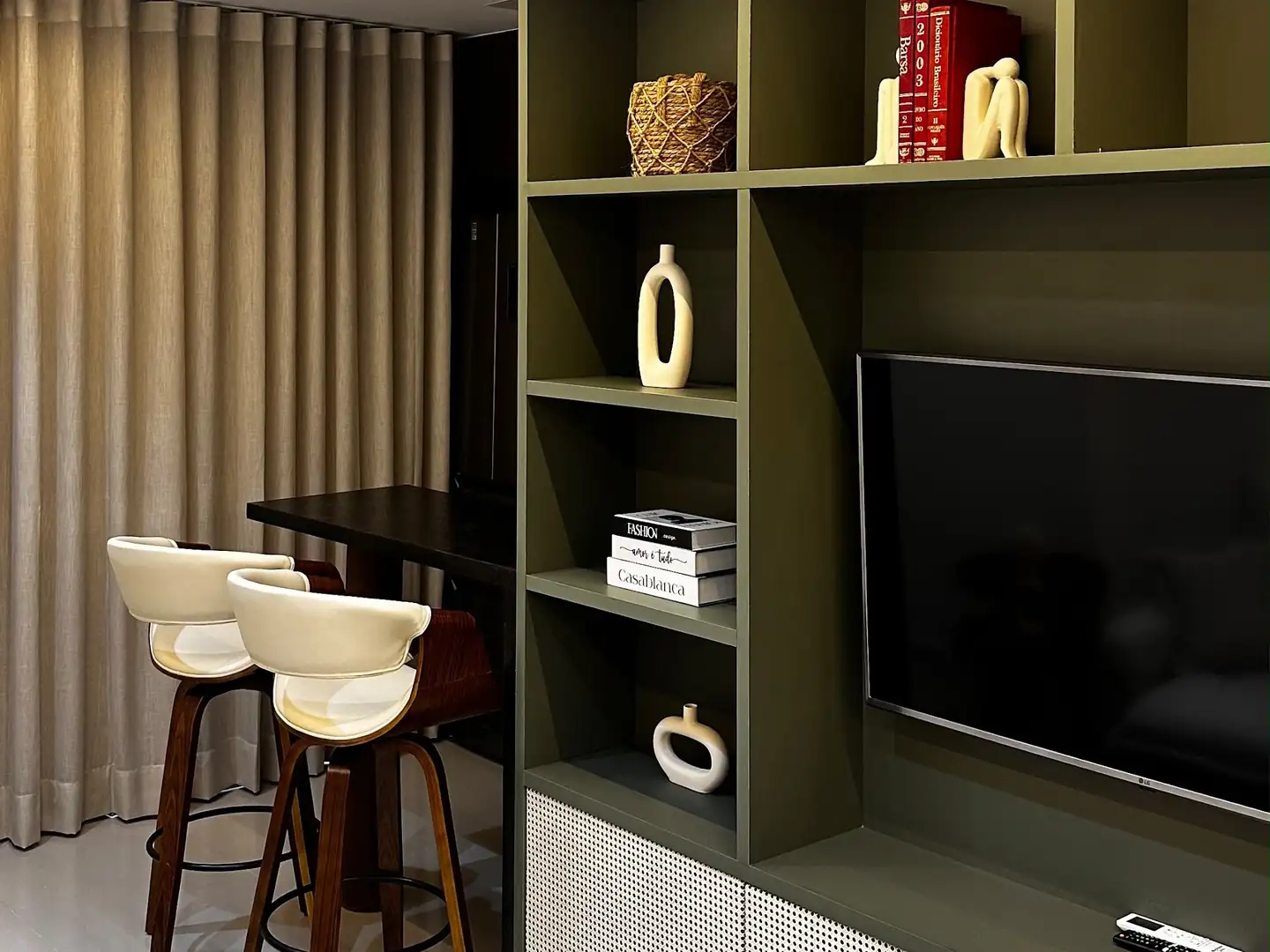 Sala de TV com cortina de tecido do teto ao piso e estante verde. Projeto da Astrale Decor