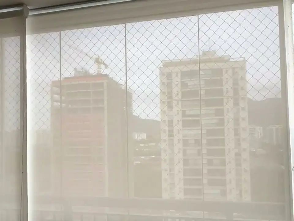 Tela solar fechada em uma varanda, com os prédios visíveis através do tecido. Projeto da Astrale Decor