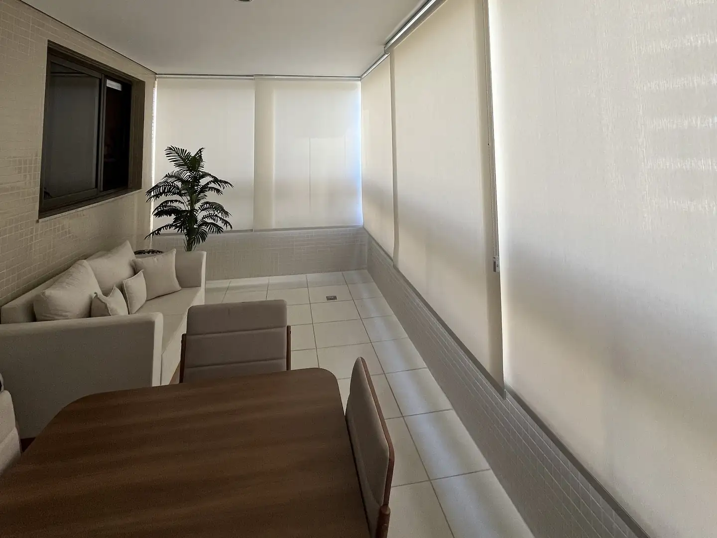 Telas solares em rolô ao longo de uma varanda com mesa e sofá